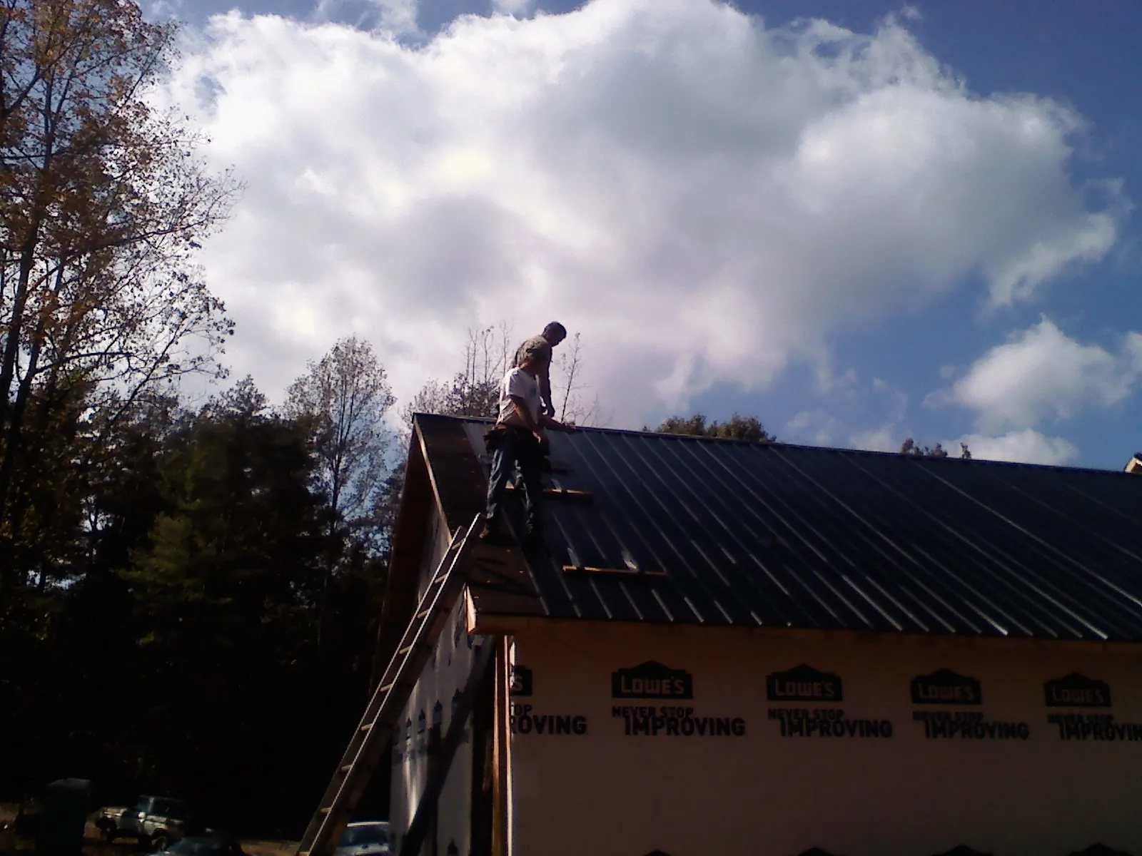 Roofer fastening dark metal panels high against a cloudy sky, from a Roof Inspection job in Philadelphia